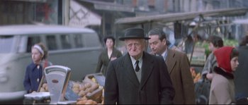 Movie still from “A Woman Is a Woman” (1961), directed by Jean-Luc Godard – An old man in a suit and a black hat; Medium shot, Over the shoulder angle