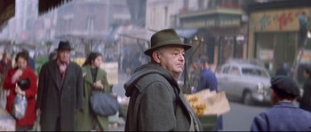 Movie still from “A Woman Is a Woman” (1961), directed by Jean-Luc Godard – An older man wearing a hat and a coat walking down the street; Medium shot, Low angle