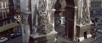 Movie still from “A Woman Is a Woman” (1961), directed by Jean-Luc Godard – A statue of a man and a woman on a pedestal in an alley; Extreme Wide shot, Overhead angle