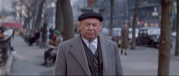 Movie still from “A Woman Is a Woman” (1961), directed by Jean-Luc Godard – An older man wearing a hat and a suit; Medium shot, Over the shoulder angle