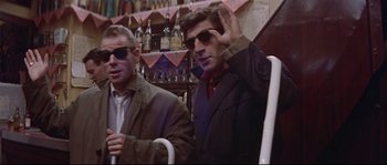 Movie still from “A Woman Is a Woman” (1961), directed by Jean-Luc Godard – Two men sitting at a bar with their hands up; Medium shot, Low angle