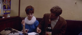Movie still from “A Woman Is a Woman” (1961), directed by Jean-Luc Godard – A man and a woman sitting next to each other at a table; Medium shot, Over the shoulder angle