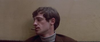 Movie still from “A Woman Is a Woman” (1961), directed by Jean-Luc Godard – A young man is smoking a cigarette while wearing a sweater; Close Up shot, Low angle