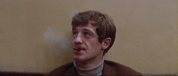 Movie still from “A Woman Is a Woman” (1961), directed by Jean-Luc Godard – A man with a mustache is smoking a cigarette; Close Up shot, Low angle
