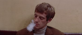 Movie still from “A Woman Is a Woman” (1961), directed by Jean-Luc Godard – A man in a brown jacket is smoking a cigarette; Close Up shot, Low angle
