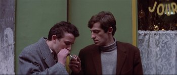 Movie still from “A Woman Is a Woman” (1961), directed by Jean-Luc Godard – Two men looking at each other while holding a cell phone; Medium shot, Low angle