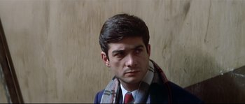 Movie still from “A Woman Is a Woman” (1961), directed by Jean-Luc Godard – A man wearing a suit and tie with a scarf around his neck; Close Up shot, Over the shoulder angle