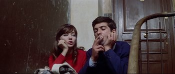 Movie still from “A Woman Is a Woman” (1961), directed by Jean-Luc Godard – A man and a woman sitting next to each other smoking; Medium shot, High angle