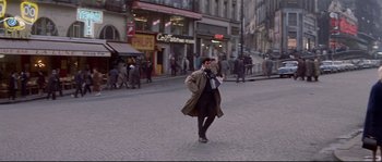 Movie still from “A Woman Is a Woman” (1961), directed by Jean-Luc Godard – A man walking down the street wearing a brown coat; Wide shot, High angle