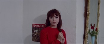 Movie still from “A Woman Is a Woman” (1961), directed by Jean-Luc Godard – A woman in a red shirt holding her hair; Medium shot, Low angle
