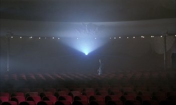 Movie still from “A Zed & Two Noughts” (1985), directed by Peter Greenaway – A person sitting in a theater with a projector; Extreme Wide shot, Low angle