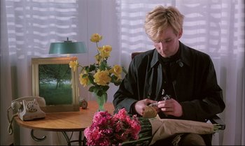 Movie still from “A Zed & Two Noughts” (1985), directed by Peter Greenaway – A person sitting at a table with a vase of flowers; Medium shot, High angle