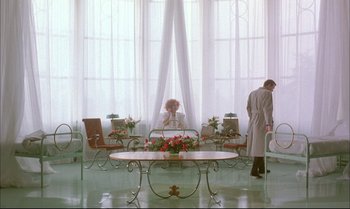 Movie still from “A Zed & Two Noughts” (1985), directed by Peter Greenaway – A man and a woman sitting at a dining room table; Wide shot, Low angle