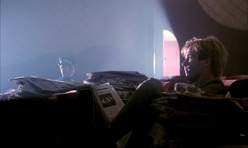 Movie still from “A Zed & Two Noughts” (1985), directed by Peter Greenaway – Two people are sitting on a couch in a dark room; Wide shot, Low angle