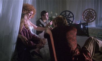 Movie still from “A Zed & Two Noughts” (1985), directed by Peter Greenaway – A group of people sitting on a couch in front of a projector; Wide shot, Over the shoulder angle