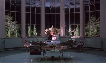 Movie still from “A Zed & Two Noughts” (1985), directed by Peter Greenaway – A woman sitting on a chair in front of a window; Wide shot, Low angle