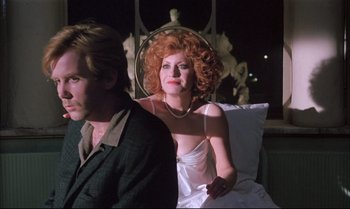 Movie still from “A Zed & Two Noughts” (1985), directed by Peter Greenaway – A man and a woman sitting next to each other; Medium shot, Low angle