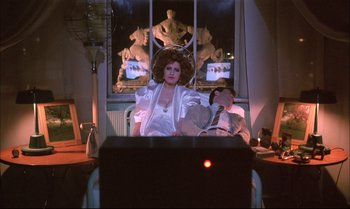 Movie still from “A Zed & Two Noughts” (1985), directed by Peter Greenaway – A man and a woman sitting in front of a television; Medium shot, Low angle