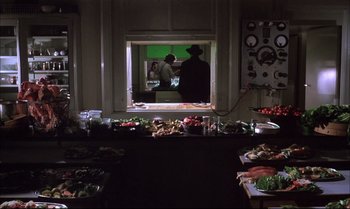 Movie still from “A Zed & Two Noughts” (1985), directed by Peter Greenaway – A room filled with lots of food on top of a table; Wide shot, High angle