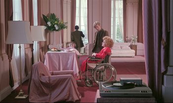 Movie still from “A Zed & Two Noughts” (1985), directed by Peter Greenaway – An older woman in a wheel chair in a living room; Wide shot, High angle