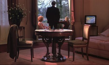 Movie still from “A Zed & Two Noughts” (1985), directed by Peter Greenaway – Two women and a man sitting in front of a window; Wide shot, Low angle