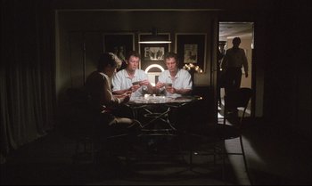Movie still from “A Zed & Two Noughts” (1985), directed by Peter Greenaway – A group of men sitting at a table in a dark room; Wide shot, Over the shoulder angle