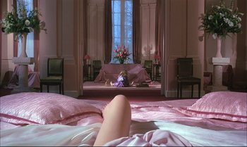 Movie still from “A Zed & Two Noughts” (1985), directed by Peter Greenaway – A woman laying on a bed in front of a large window; Wide shot, High angle