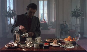 Movie still from “A Zed & Two Noughts” (1985), directed by Peter Greenaway – A man pouring tea into a cup on a table; Medium shot, Low angle