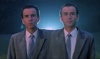 Movie still from “A Zed & Two Noughts” (1985), directed by Peter Greenaway – A man wearing a suit and tie standing next to another man wearing a suit and tie standing next to each other; Medium shot, Low angle