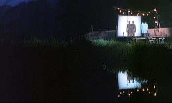 Movie still from “A Zed & Two Noughts” (1985), directed by Peter Greenaway – Two men standing in front of a screen at night near a pond; Extreme Wide shot, Low angle