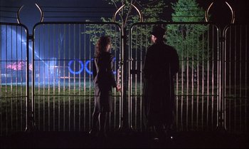 Movie still from “A Zed & Two Noughts” (1985), directed by Peter Greenaway – A man and a woman standing in front of a gate; Wide shot, Over the shoulder angle