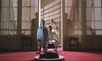 Movie still from “A Zed & Two Noughts” (1985), directed by Peter Greenaway – A group of people standing in front of an open door; Wide shot, Low angle