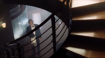 Movie still from “A.I. Artificial Intelligence” (2001), directed by Steven Spielberg – A man in a suit and bow tie standing in front of a spiral staircase; Wide shot, Low angle