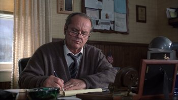 Movie still from “About Schmidt” (2002), directed by Alexander Payne – An older man writing on a piece of paper at a desk; Medium shot, Low angle