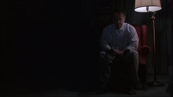 Movie still from “About Schmidt” (2002), directed by Alexander Payne – A man sitting on a chair in a dark room; Wide shot, Low angle