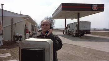 Movie still from “About Schmidt” (2002), directed by Alexander Payne – A man standing in front of a gas station talking on a phone; Medium shot, Low angle