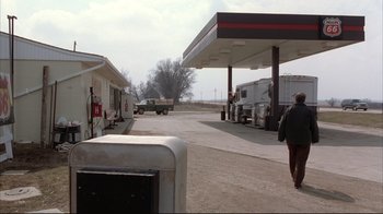 Movie still from “About Schmidt” (2002), directed by Alexander Payne – A man walking down a street next to a gas station; Extreme Wide shot, Over the shoulder angle