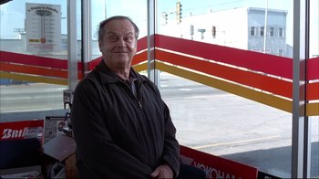 Movie still from “About Schmidt” (2002), directed by Alexander Payne – An older man sitting in front of a store window; Medium shot, Low angle