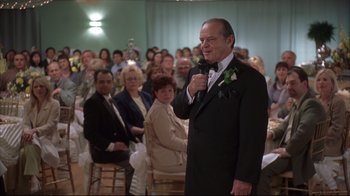 Movie still from “About Schmidt” (2002), directed by Alexander Payne – A man in a suit is giving a speech to a group of people; Medium shot, Over the shoulder angle