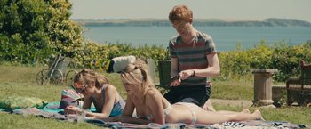 Movie still from “About Time” (2013), directed by Richard Curtis – A group of people laying on a blanket near a body of water; Medium shot, High angle