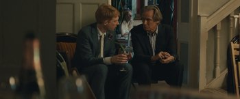 Movie still from “About Time” (2013), directed by Richard Curtis – Two men in suits are sitting next to each other; Medium shot, Over the shoulder angle
