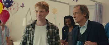 Movie still from “About Time” (2013), directed by Richard Curtis – A group of people standing next to each other in a room; Medium shot, Over the shoulder angle