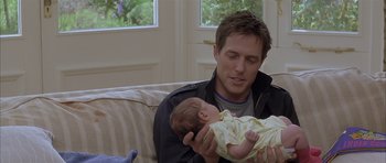 Movie still from “About a Boy” (2002), directed by Chris Weitz – A man holding a baby on a couch; Medium shot, Over the shoulder angle