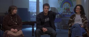 Movie still from “About a Boy” (2002), directed by Chris Weitz – A man sitting on a chair in a living room; Medium shot, Over the shoulder angle