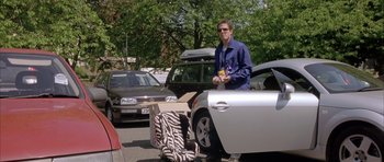 Movie still from “About a Boy” (2002), directed by Chris Weitz – A man standing next to a car with boxes on it; Wide shot, Low angle