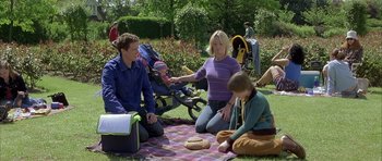 Movie still from “About a Boy” (2002), directed by Chris Weitz – A group of people sitting on a blanket in the grass; Medium shot, High angle