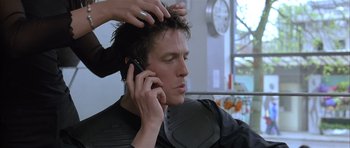 Movie still from “About a Boy” (2002), directed by Chris Weitz – A man talking on a cell phone while getting his hair combed; Close Up shot, Over the shoulder angle