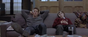 A man and a boy sitting on a couch with their hands behind their heads
