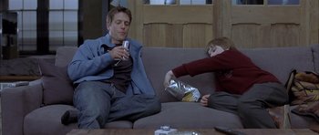 Movie still from “About a Boy” (2002), directed by Chris Weitz – Two people sitting on a couch eating food and drinking wine; Medium shot, Over the shoulder angle