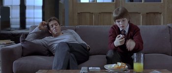 Movie still from “About a Boy” (2002), directed by Chris Weitz – A man and a boy sitting on a couch looking at a cell phone; Medium shot, Low angle